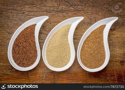 three tiny gluten free grains - kaniwa, amaranth and teff on teardrop shaped bowls against rustic wood