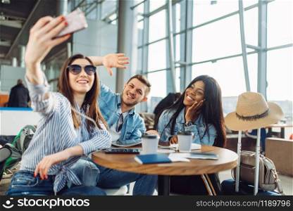 Three tourists makes selfie on phone in airport. Passengers with baggage look forward to flight in air terminal, happy friends on journey, summer travel on vacation