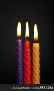 three twisted burning candles over black background