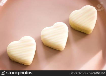 Three white chocolate hearts on a pink background