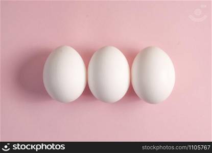 Three white eggs on a pink background. Group of three eggs.