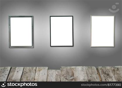 Three white isolated wooden frames on the gray wall with wooden desk