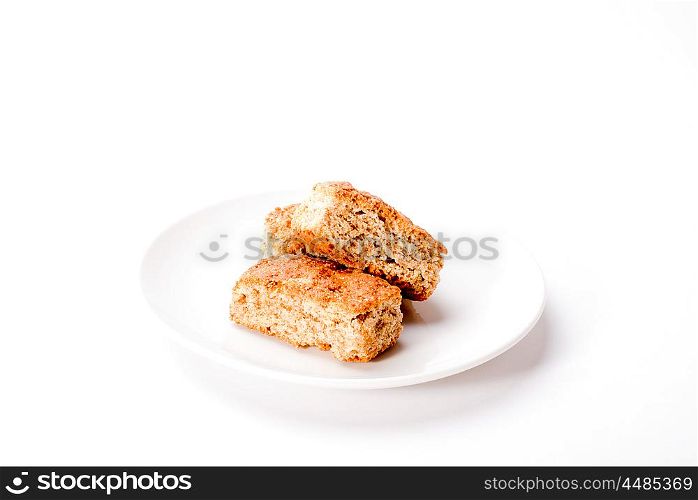 Three whole grain rusks are stacked on a white plate and situated on a white background.
