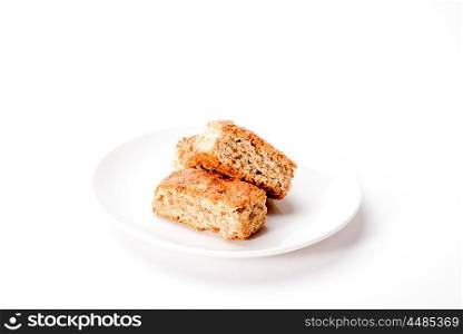 Three whole grain rusks are stacked on a white plate and situated on a white background.