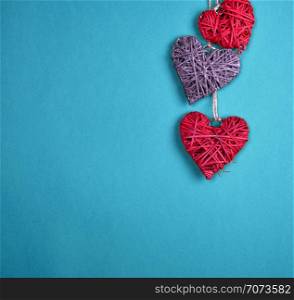 three wicker hearts hang on a rope, blue background, copy space
