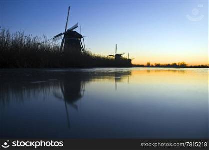 Three windmills near an ice covered frozen canal during a winter dawn in Leidschendam, the Netherlands