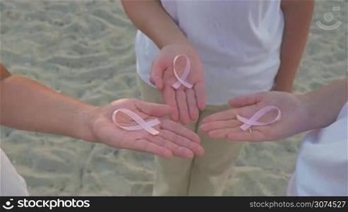 Three woman holding pink breast cancer awareness ribbons in hands. Support and solidarity in taking with disease