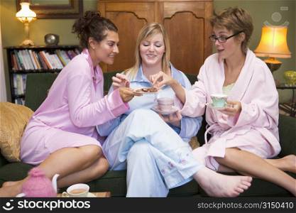 Three woman in night clothes sitting at home eating cookies and drinking tea
