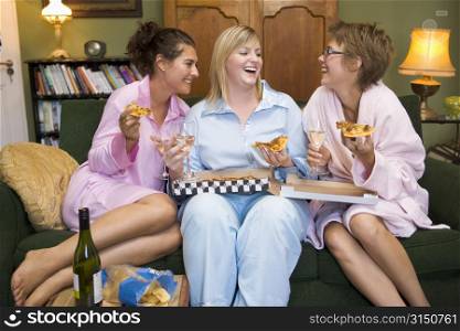 Three woman in night clothes sitting at home eating pizza