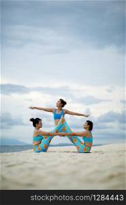 three woman playing yoga pose on sand beach