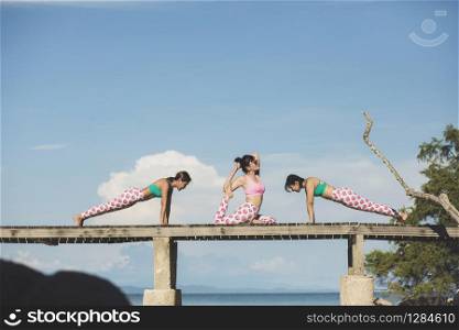 three woman vacation relaxing and playing yoga pose on beach pier