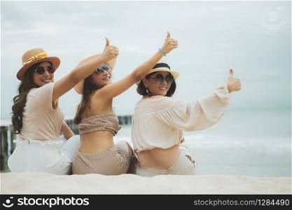 three woman wearing straw hat sitting on vacation beach rising good thumb
