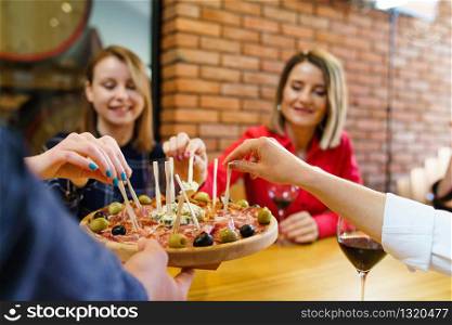 Three women caucasian girls sitting by the table holding glasses of red wine while unknown man is serving appetizer friends smiling in day at home or restaurant