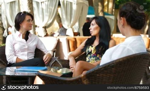 Three women enjoy a coffee break at outdoor cafe, chatting together