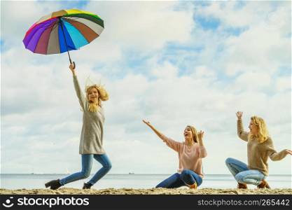 Three women full of joy having great time together. One woman holding colorful umbrella.. Women holding umbrella having fun with friends