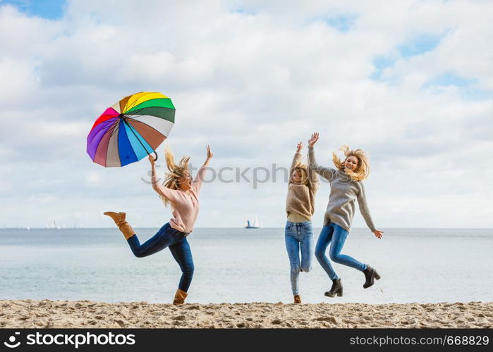 Three women full of joy jumping around with colorful umbrella. Female friends having fun outdoor.. Women jumping with umbrella