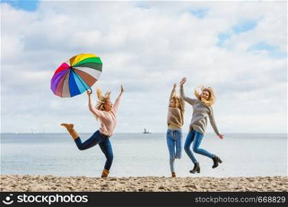 Three women full of joy jumping around with colorful umbrella. Female friends having fun outdoor.. Women jumping with umbrella
