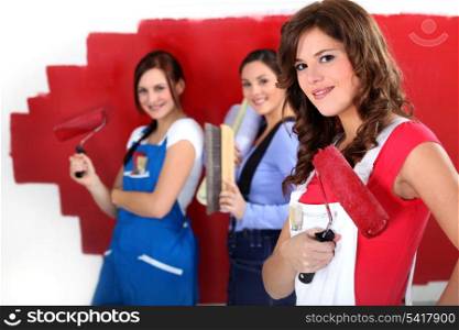 Three women painting a wall in red.