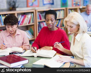 Three women sitting in library with books and notepads (selective focus)