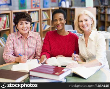 Three women sitting in library with books and notepads (selective focus)