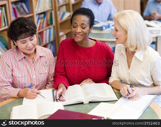 Three women sitting in library with books and notepads (selective focus)