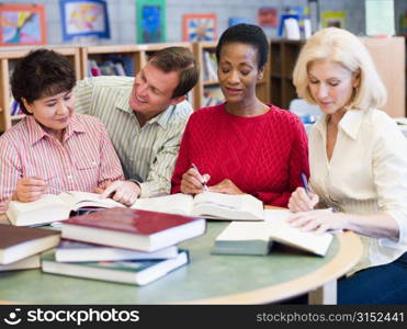 Three women sitting in library with books and notepads while a man leans over them (selective focus)