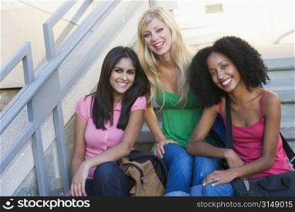 Three women sitting on staircase outdoors smiling (high key)