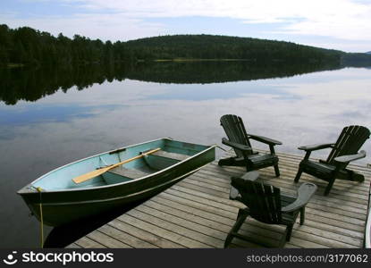 Three wooden adirondack chairs on a boat dock on a beautiful lake in the evening