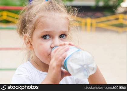 Three year old girl drinks from a bottle. Three year old girl drinks from a bottle at the playground