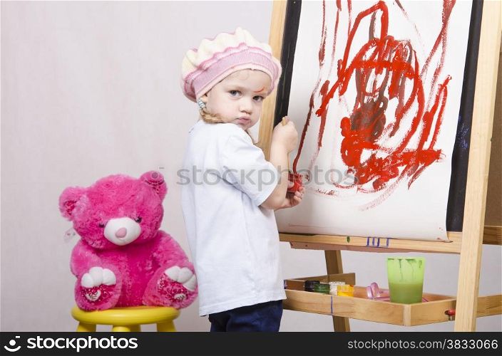 Three-year-old girl playing in the artist. Girl draws on the easel paints bear sitting on a chair