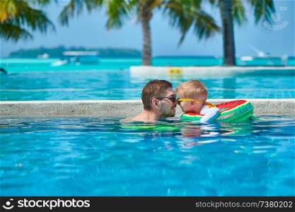 Three year old toddler boy in resort swimming pool eskimo kissing his father. Summer family vacation at Maldives.