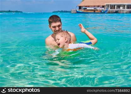 Three year old toddler boy learns to swim with father. Summer family vacation at Maldives.