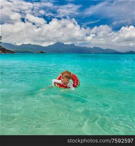 Three year old toddler boy on beach at Seychelles swimming with inflatable ring