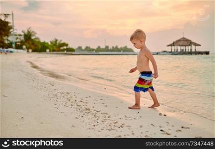 Three year old toddler boy on beach at sunset. Summer family vacation at Maldives.