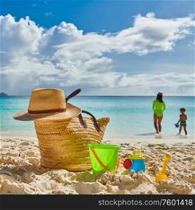 Three year old toddler boy on beach with mother. Beach bag and toys. Summer family vacation at Mahe, Seychelles.