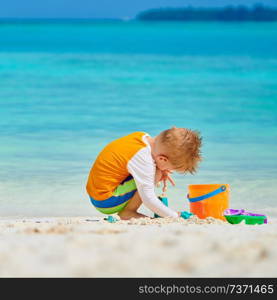 Three year old toddler boy playing with beach toys on beach.  Summer family vacation at Maldives.