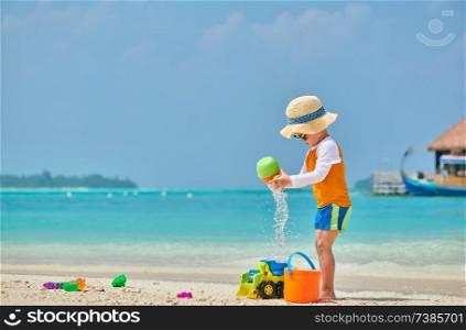 Three year old toddler boy playing with beach toys on beach. Summer family vacation at Maldives.