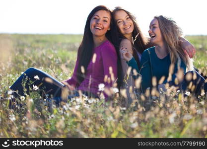 three young beautiful woman sitting in a field on the sky background