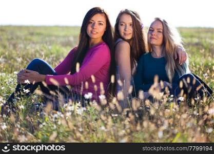 three young beautiful woman sitting in a field on the sky background