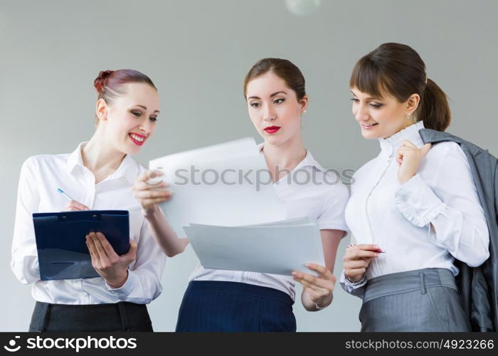 Three young businesswomen. Image of attractive businesswomen holding folders and discussing