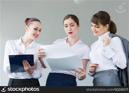 Three young businesswomen. Image of attractive businesswomen holding folders and discussing