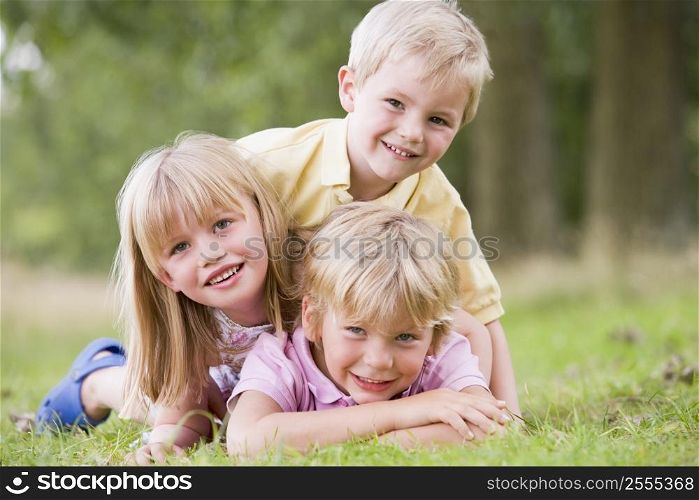 Three young children playing outdoors smiling
