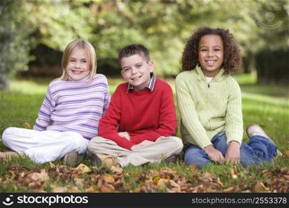 Three young children sitting outdoors smiling (selective focus)