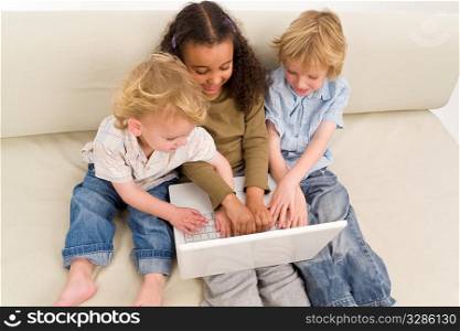 Three young children using a laptop together while sitting on a settee