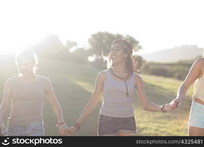 Three young females friends holding hands in sunlight