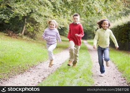 Three young friends running on a path outdoors smiling
