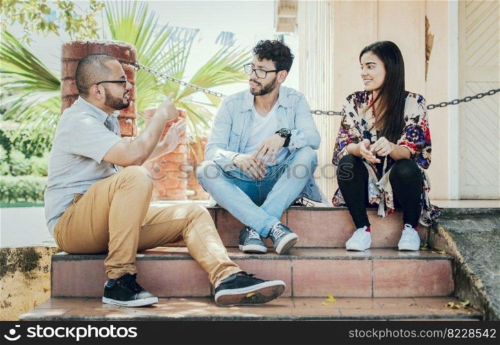 Three young friends talking sitting on the stairs. Three teenage friends talking sitting on the stairs, Three young people sitting on the street talking. Concept of friends talking