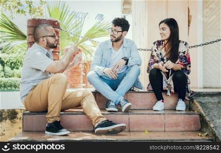 Three young friends talking sitting on the stairs. Three teenage friends talking sitting on the stairs, Three young people sitting on the street talking. Concept of friends talking