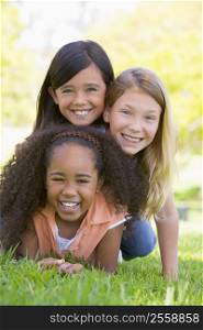 Three young girl friends piled up on top of each other outdoors smiling