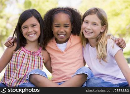 Three young girl friends sitting outdoors smiling